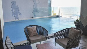 Zona de piscina con dos sillas y una mesa, vista al océano y un edificio de diseño moderno con arte en la pared.
