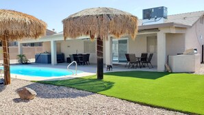 Un patio trasero con piscina, mobiliario exterior y un área de patio cubierta.