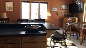 A kitchen with wooden cabinets, a dining table, chairs, a bar stool, and a television.
