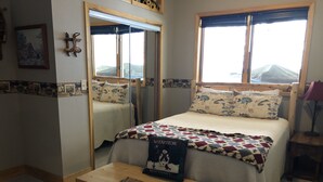 A bedroom with a bed, a wooden nightstand, a mirror, and a window with a view of mountains.