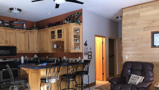 A modern kitchen with wooden cabinets, a bar area, and a leather chair with a pillow.