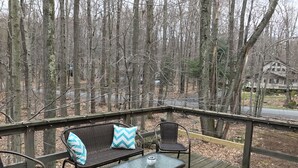 A wooden deck with wicker furniture and a glass table, overlooking a forested area.