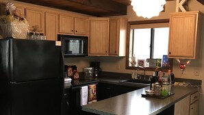A kitchen with wooden cabinets, a black refrigerator, a microwave, and a window.
