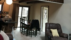 A spacious living room with a high ceiling, a wooden staircase, a dining area, and a cozy seating arrangement.