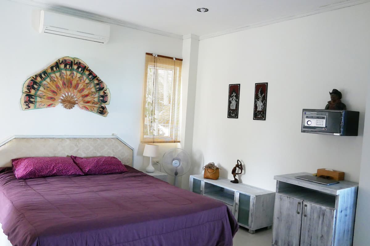 A bedroom with a bed, bedside tables, a desk, an air conditioner, and decorative items.