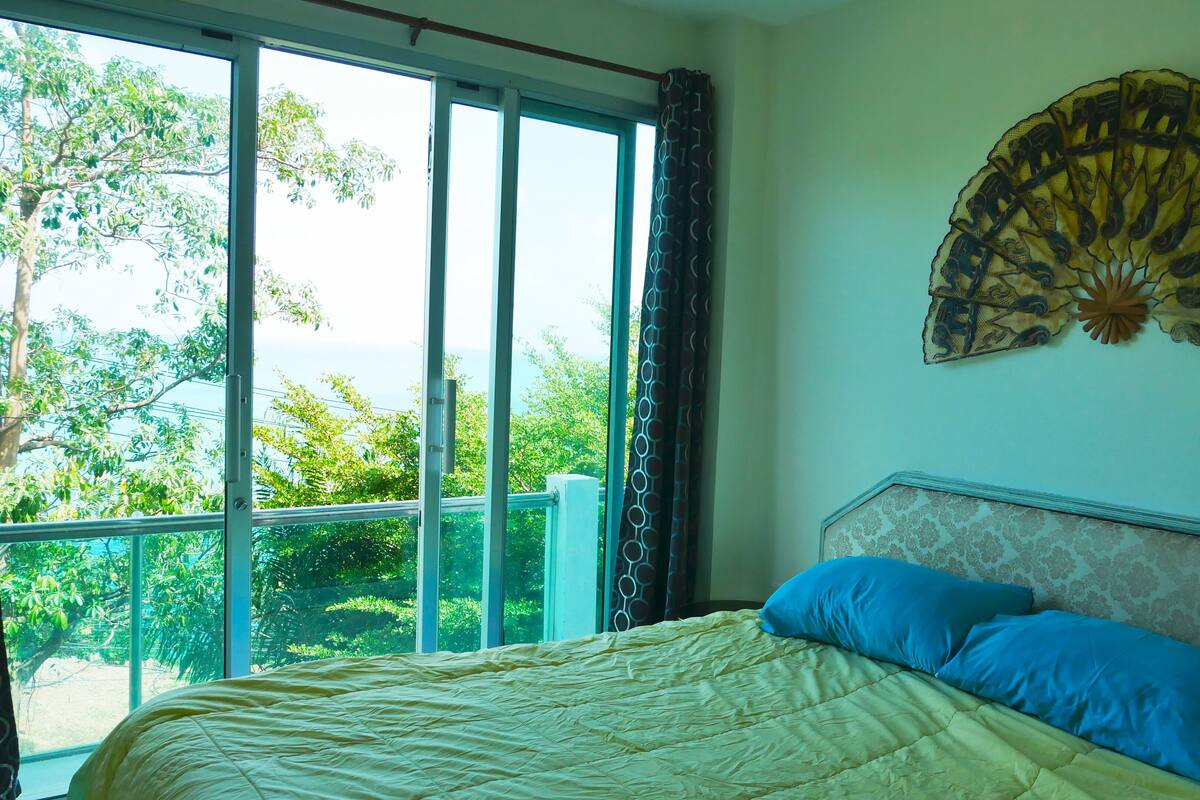 A bedroom with a large window, a bed with blue pillows, and a decorative wall piece.