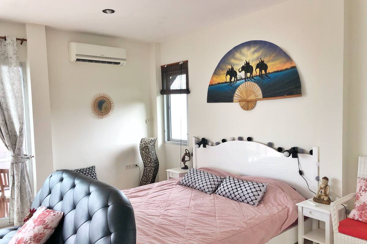 A bedroom with a bed, a chair, a nightstand, and a wall-mounted air conditioner.