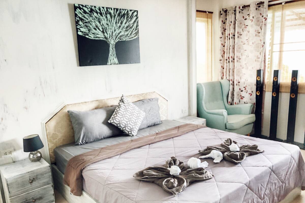 A bedroom with a bed, pillows, a nightstand, a chair, and a wall art piece.