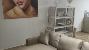 A modern living room with a beige sectional sofa, a white wall with a large painting, a wooden sideboard with decorative items, and a hanging light fixture. - Private Villa with pool. Top location, a short walk to the beach (Canggu)