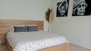 A bedroom with a wooden headboard, a patterned bedspread, and two pillows. There are two wall-mounted artworks and a tall, decorative plant. - Private Villa with pool. Top location, a short walk to the beach (Canggu)