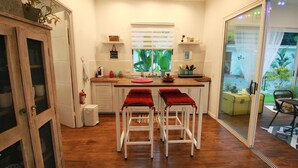 Una cocina compacta con una isla central, dos taburetes de bar, una ventana con persianas y una puerta corrediza de vidrio que da a un espacio exterior.
