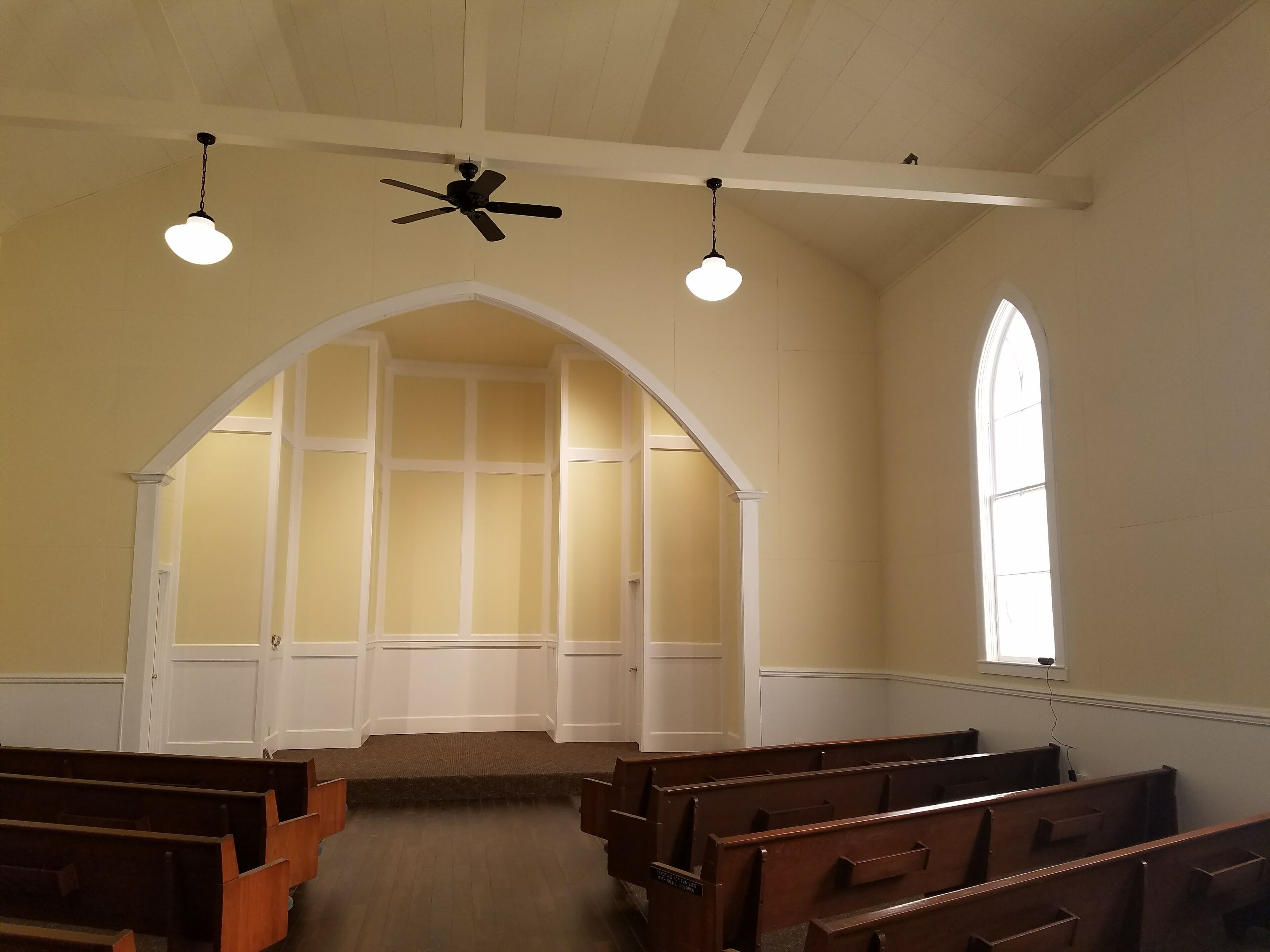 An interior with pews, a high arched doorway, and a large window.