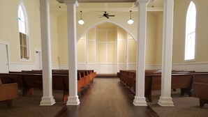 Interno di una chiesa con panche di legno, colonne bianche e soffitto alto.