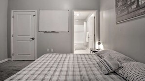 Ein Schlafzimmer mit einem Bett, einer Whiteboard-Tafel, einer Tür und einem Flur, der zu einem Badezimmer führt.