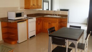 A compact kitchen with wooden cabinets, a microwave, a stove, a sink, and a dining table with chairs. - Comfy Villa Suites in Long Bay Beach (Long Bay Hills)