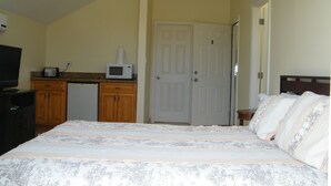 A bedroom with a bed, a television, a microwave, and a door. - Comfy Villa Suites in Long Bay Beach (Long Bay Hills)