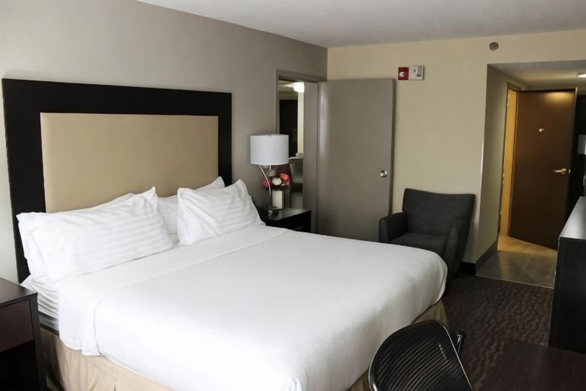 A hotel room with a large bed, a desk, a chair, and a door.