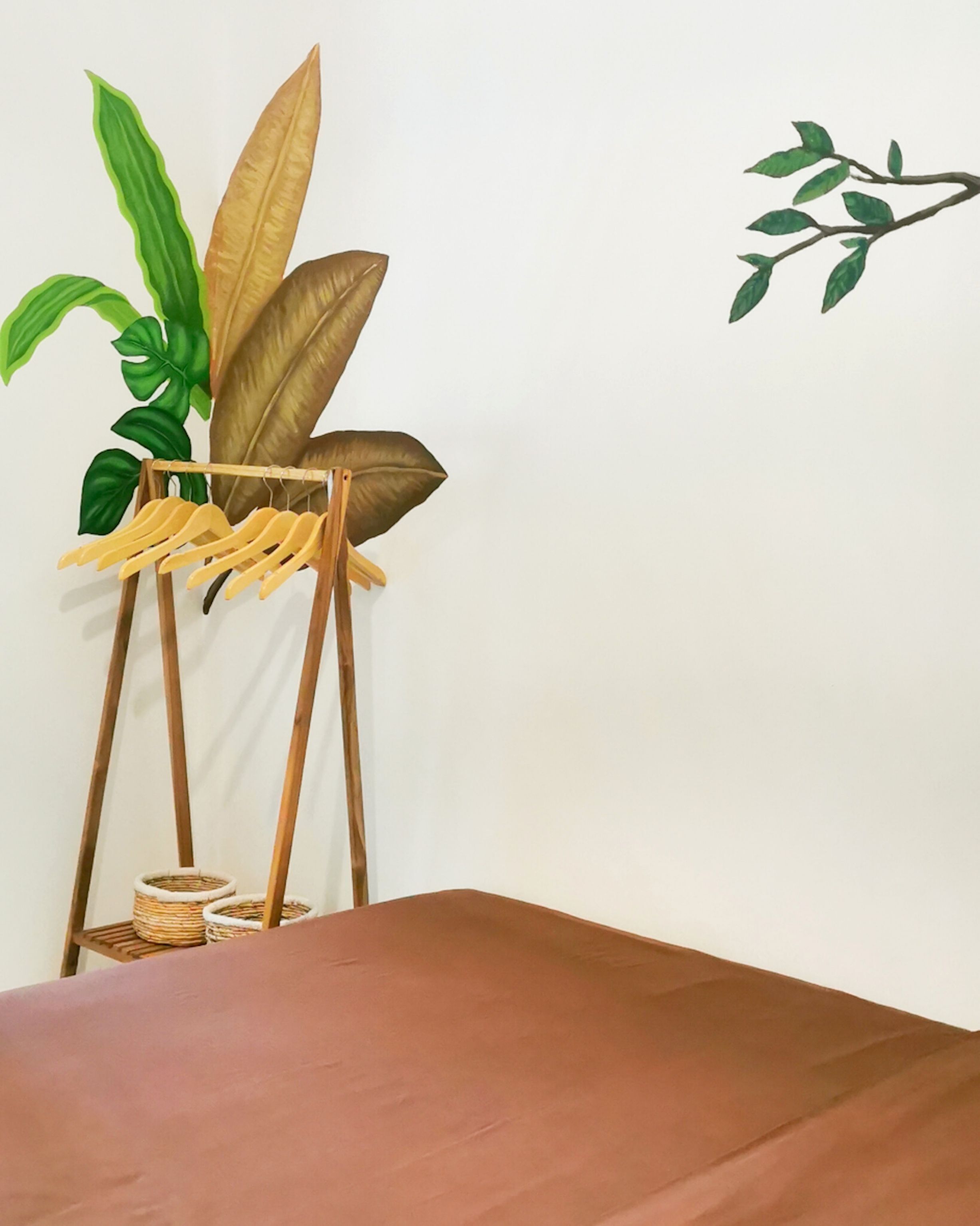 Ein Zimmer mit einem Bett, einem Kleiderständer aus Holz mit Kleidung und einer Topfpflanze.