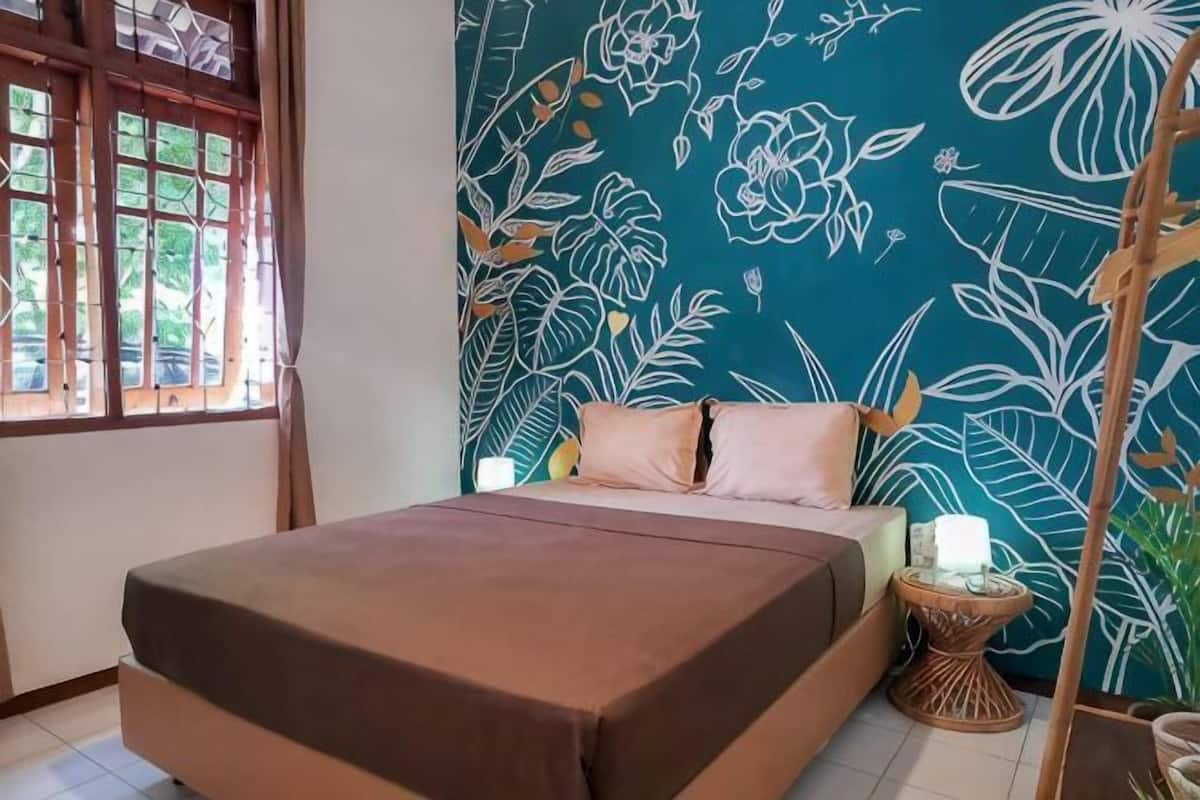 A bed with a brown bedspread, a bedside table with a white lamp, and a wall with a floral pattern.