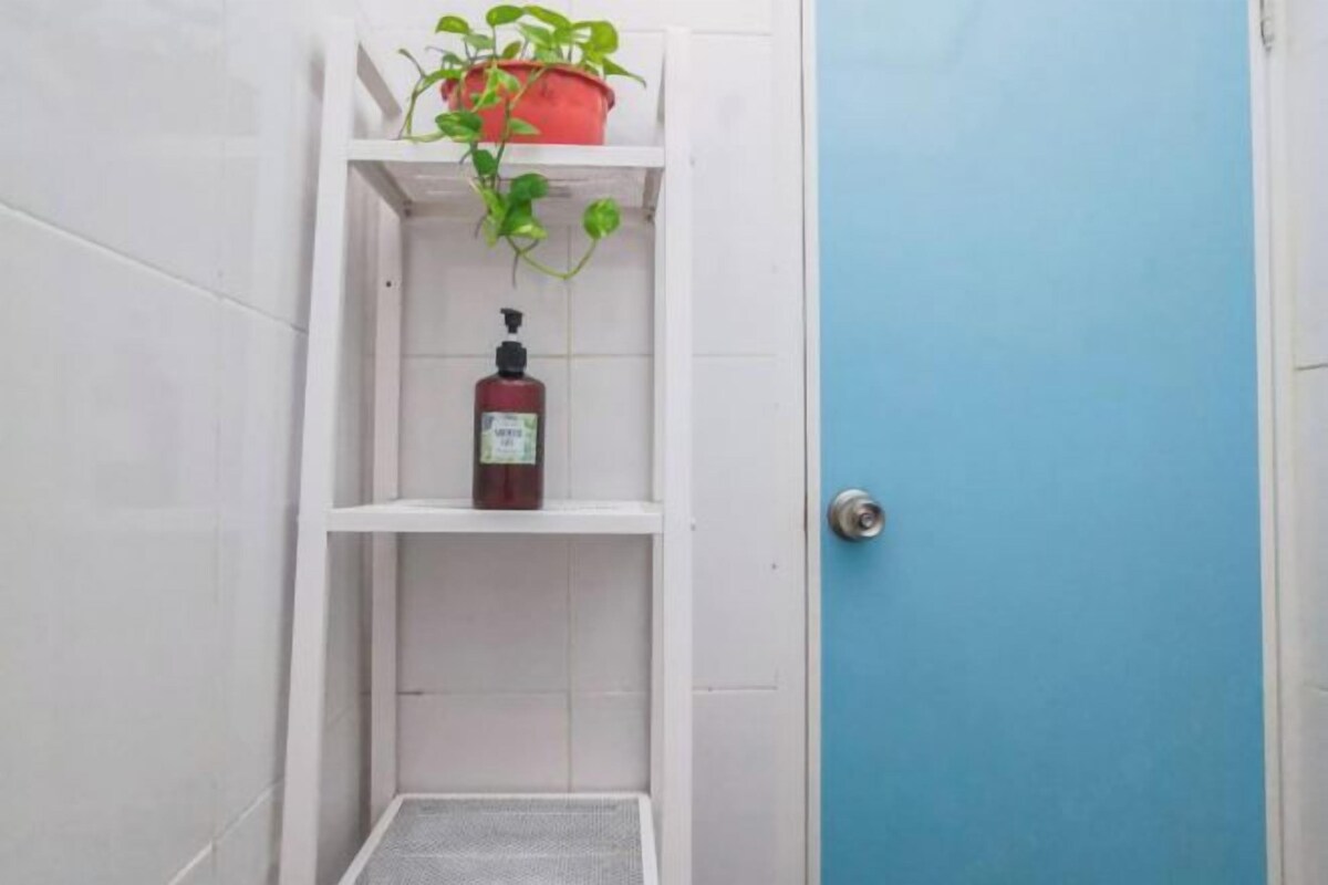 A bathroom with white tiles, a blue door, a shelf with a potted plant, and a bottle of shampoo.