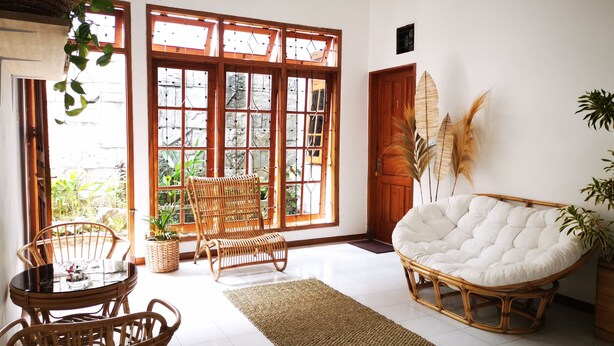 Una habitación con un gran ventanal, muebles de mimbre y una silla blanca acolchada.