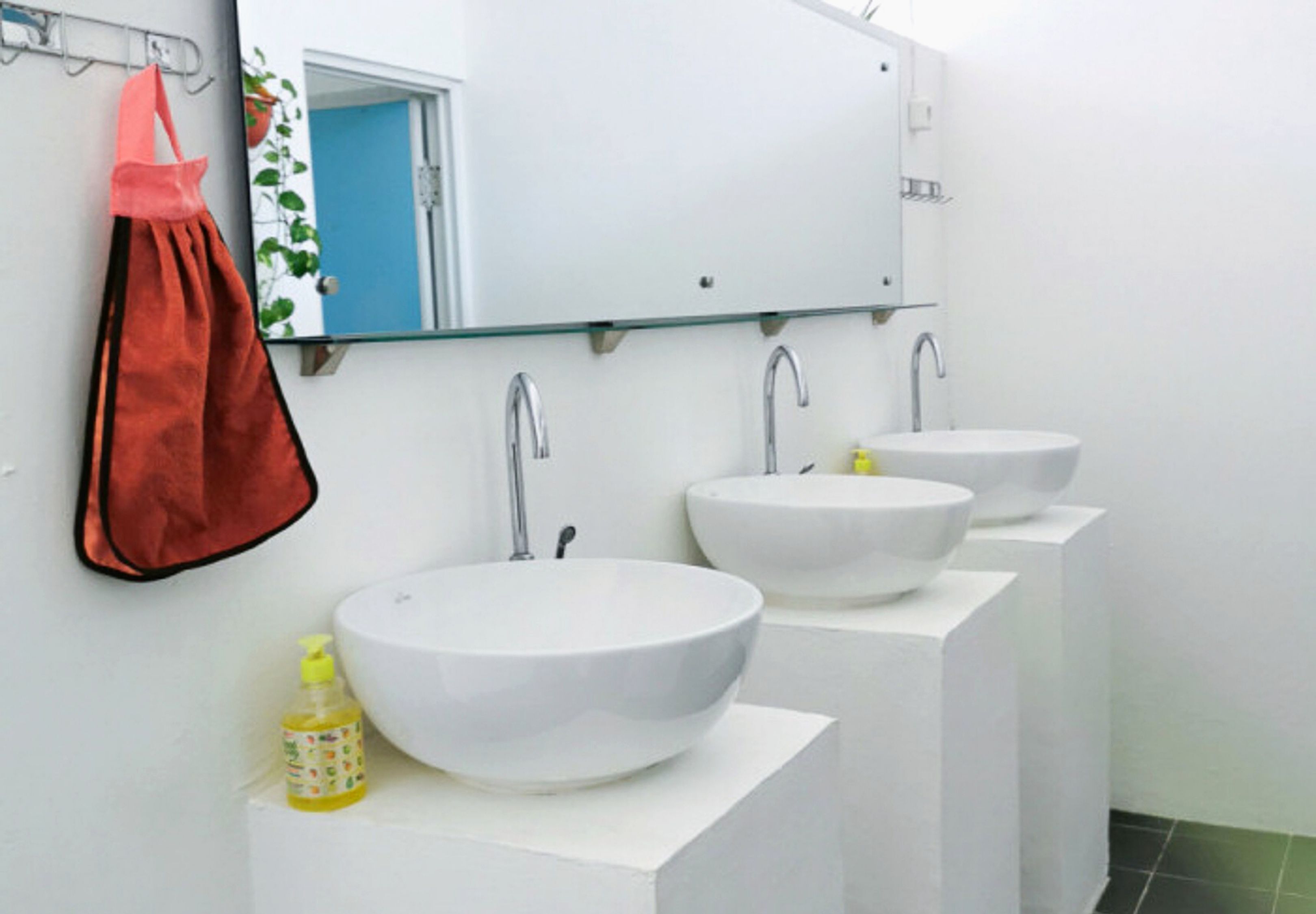 A bathroom with three white sinks, a glass mirror, and a red towel hanging on the wall.