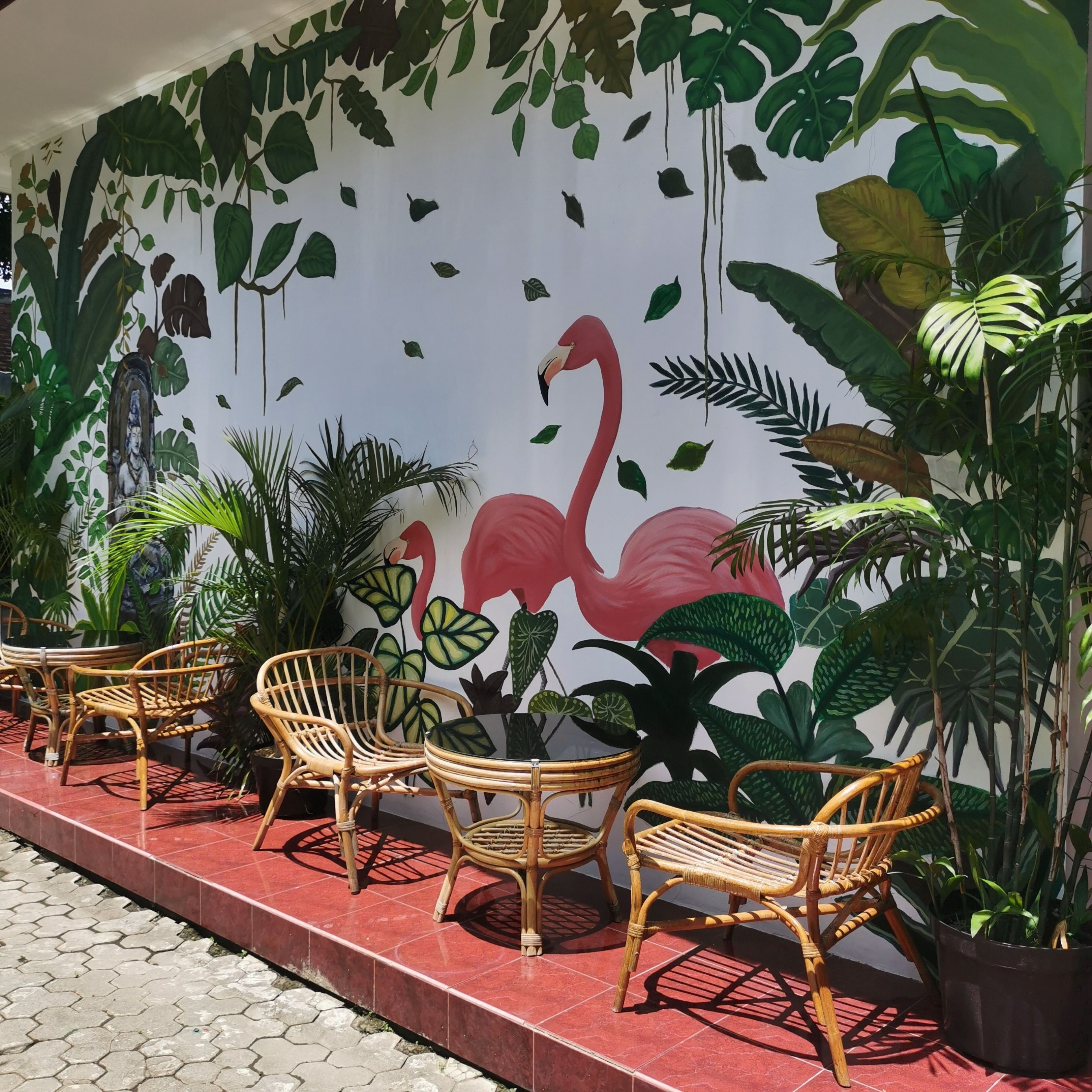 Un espace détente avec des fauteuils en osier et une table, une fresque représentant des flamants roses et des feuilles tropicales, ainsi que des plantes en pot.