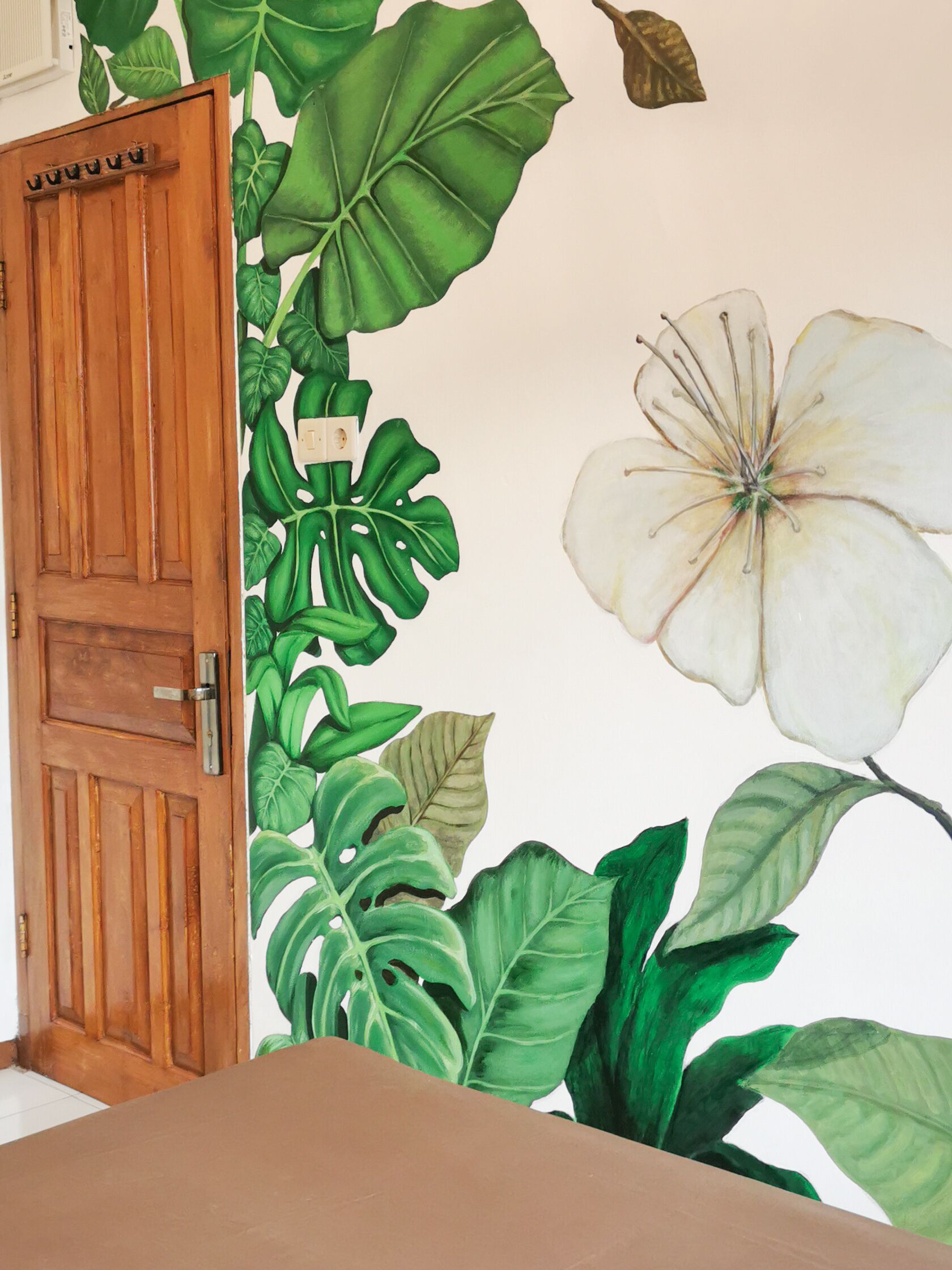A room with a wooden door, a large white flower mural, and green foliage artwork on the wall.