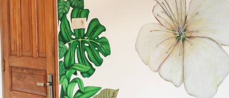 A room with a wooden door, a large white flower mural, and green foliage artwork on the wall.