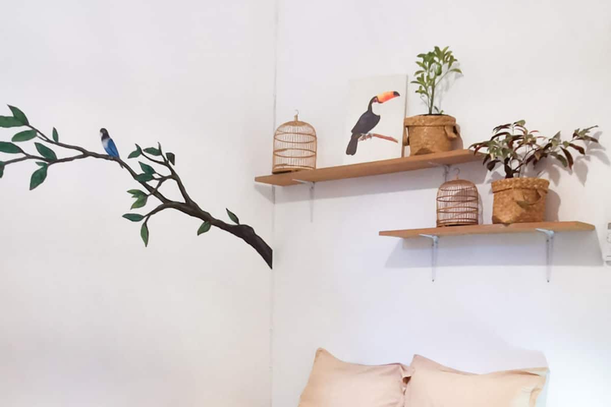 A bedroom with a bed, pillows, a branch wall decal, and two shelves with decorative items.
