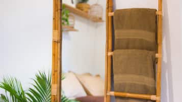 A mirror with a wooden frame reflecting a room with a brown towel hanging on the wall, a plant, and a shelf with decorative items.