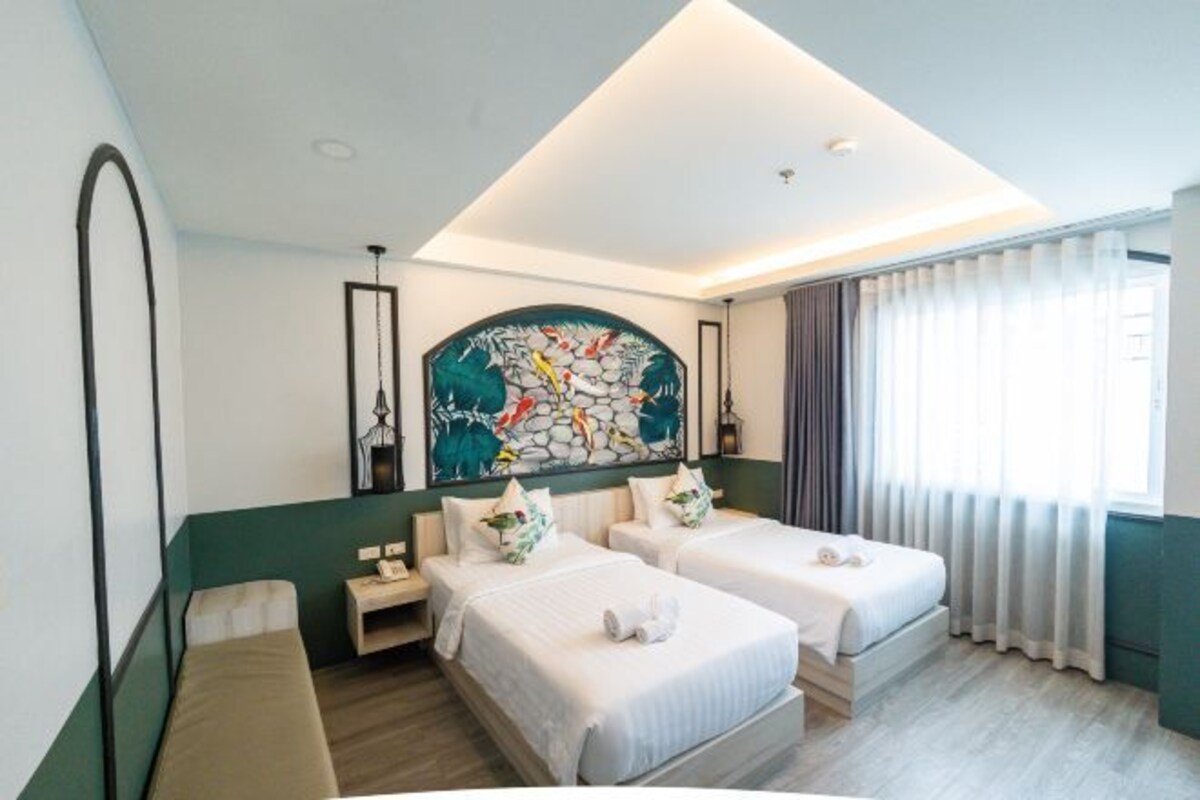 Une chambre d’hôtel avec deux lits, une grande peinture abstraite au mur, une fenêtre avec des rideaux et une petite table de chevet avec une lampe.
