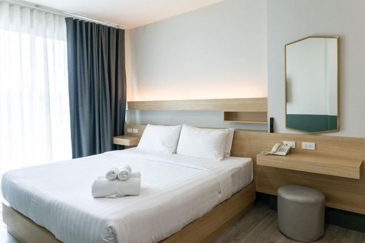 A hotel room with a large bed, a bedside table with a phone, a mirror, and a small stool.