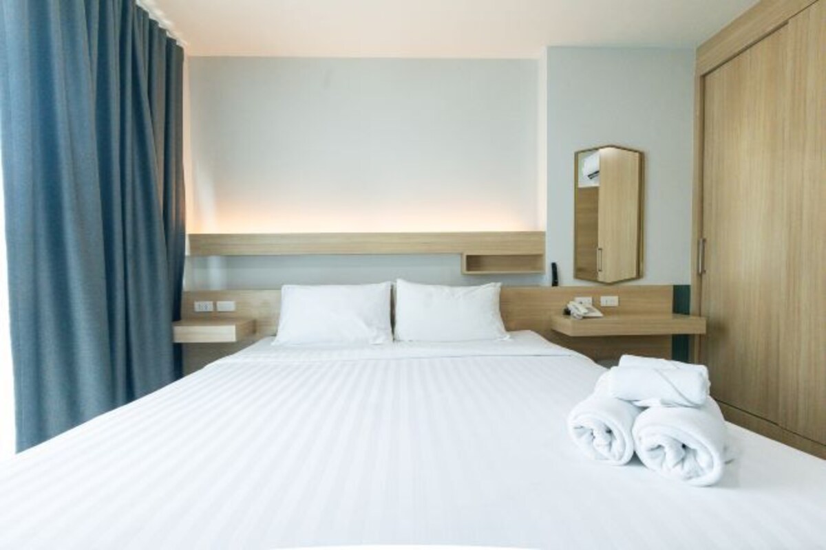 Une chambre d’hôtel avec un grand lit, une armoire en bois, une table de chevet avec une lampe et un miroir au mur.