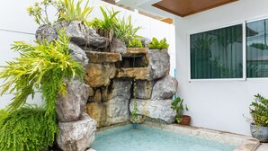 A rock garden with a small pool, surrounded by various plants and a large window. - Peranakan House (Wichit)