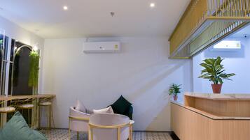 A modern reception area with a wooden desk, two white chairs, a green sofa, and a staircase with a yellow railing.