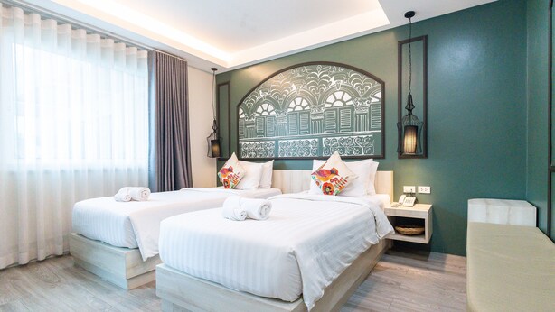 A hotel room with two beds, a bedside table with a lamp, and a chair. - Peranakan House (Wichit)