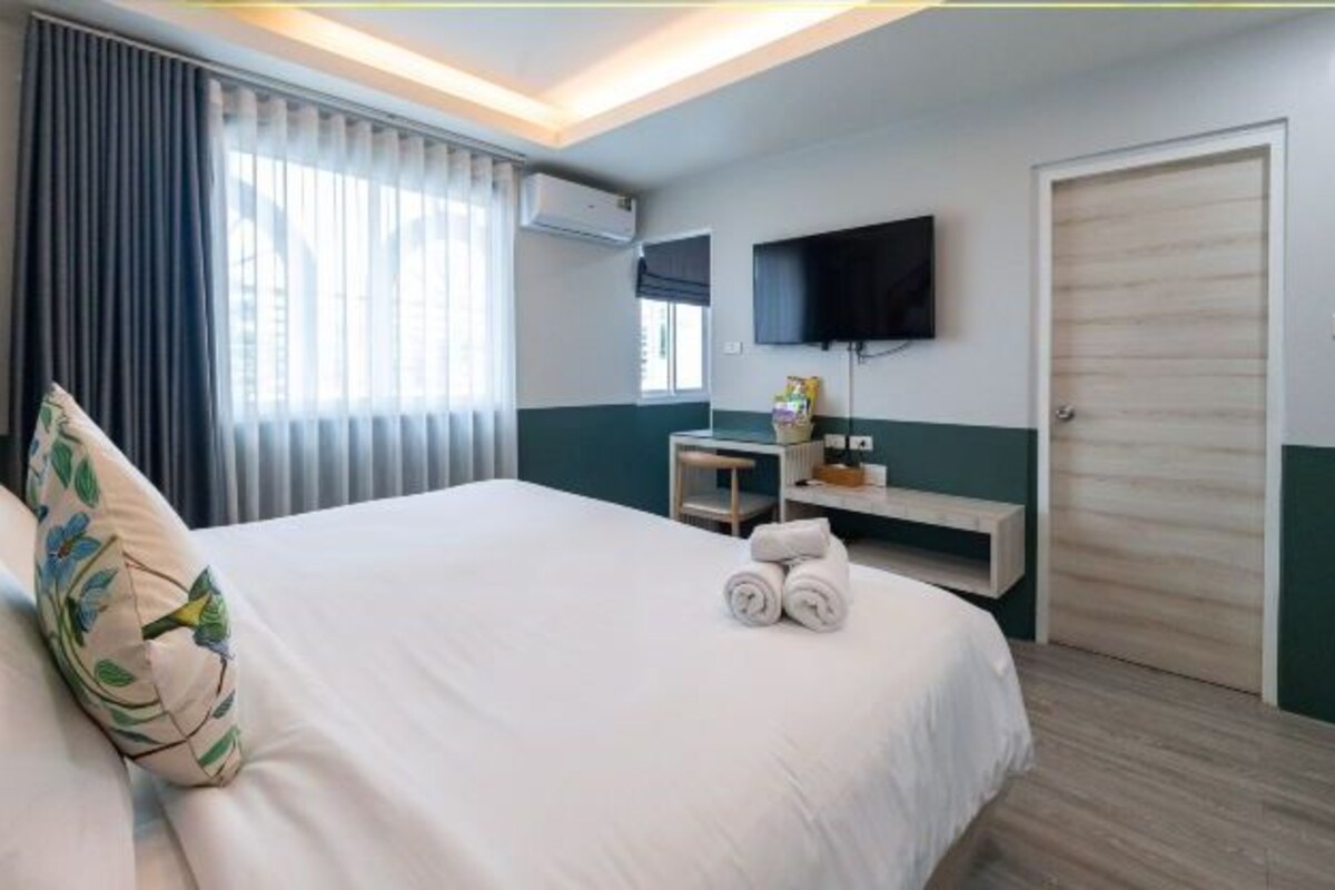 Une chambre d’hôtel avec un grand lit, un téléviseur fixé au mur, un bureau avec une chaise et une porte.