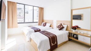 A hotel room with two beds, a TV, a coffee maker, and a view of buildings outside the window. - Moschino HT (Nha Trang)
