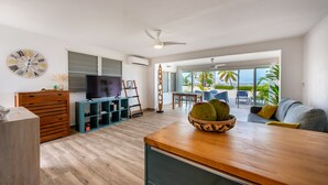 Una sala de estar moderna con una mesa de centro de madera, un televisor y un amplio ventanal con vistas a un balcón con mobiliario exterior.