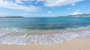 Una playa con agua turquesa cristalina, olas suaves y una isla a lo lejos.