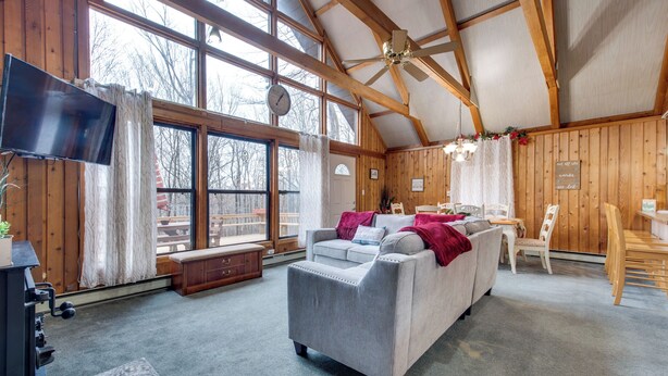 A spacious living room with a large gray sofa, a wooden ceiling, and a television mounted on the wall. - Fire Pit + Community Perks: Gouldsboro Cabin! (Gouldsboro)
