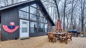 A wooden deck with a table and chairs, a barbecue grill, and a building with large windows and a door. - Fire Pit + Community Perks: Gouldsboro Cabin! (Gouldsboro)