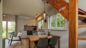 A modern kitchen with wooden cabinets, a dining area with a wooden table and chairs, and a view of the outdoors through large windows.