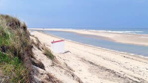 A sandy beach with a white structure with a red roof, likely a lifeguard station, and a clear blue sky.
