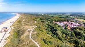 An aerial view of a coastal town with a beach, a winding road, and a cluster of houses with red roofs.