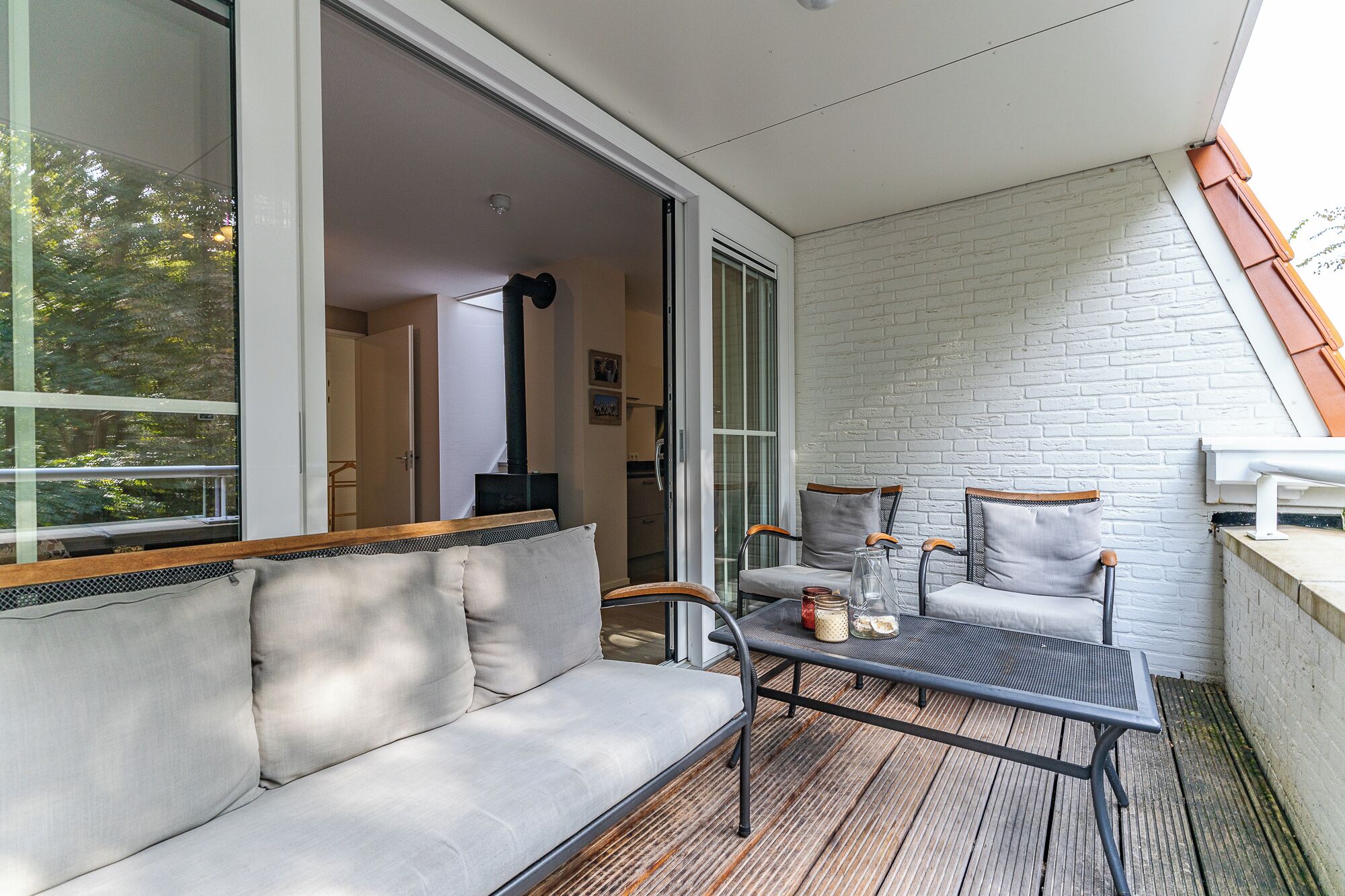 A balcony with a sofa, two chairs, a table, and a view of the interior through glass doors.
