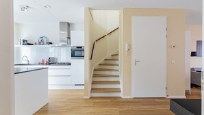 Et moderne køkken med hvide skabe, en indbygget ovn og en trætrap, der fører til et andet rum.