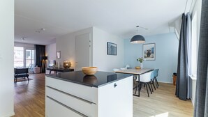 Et moderne køkken med en central ø, et spiseområde med bord og stole, samt udsigt over byen gennem store vinduer.
