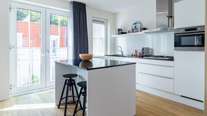 Et moderne køkken med en central ø, barstole, indbygget ovn og et stort vindue.